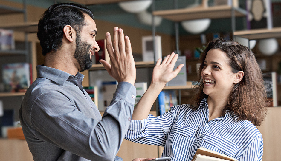 Ein Mann und eine Frau geben sich ein High-Five und lächeln dabei.