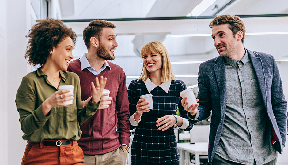 Zwei Frauen und zwei Männer im Casual Business Look stehen mit Kaffeebechern nebeneinander und unterhalten sich