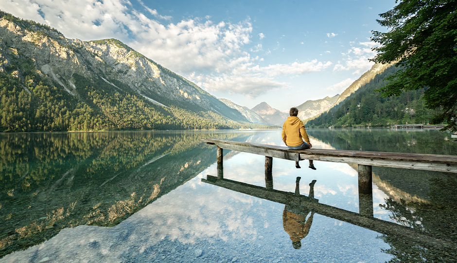 Ein Mann sitzt auf einer Bank an einem See in den Bergen