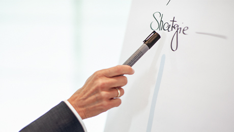 Eine Hand weist mit einem Filzstift auf ein Flipchart